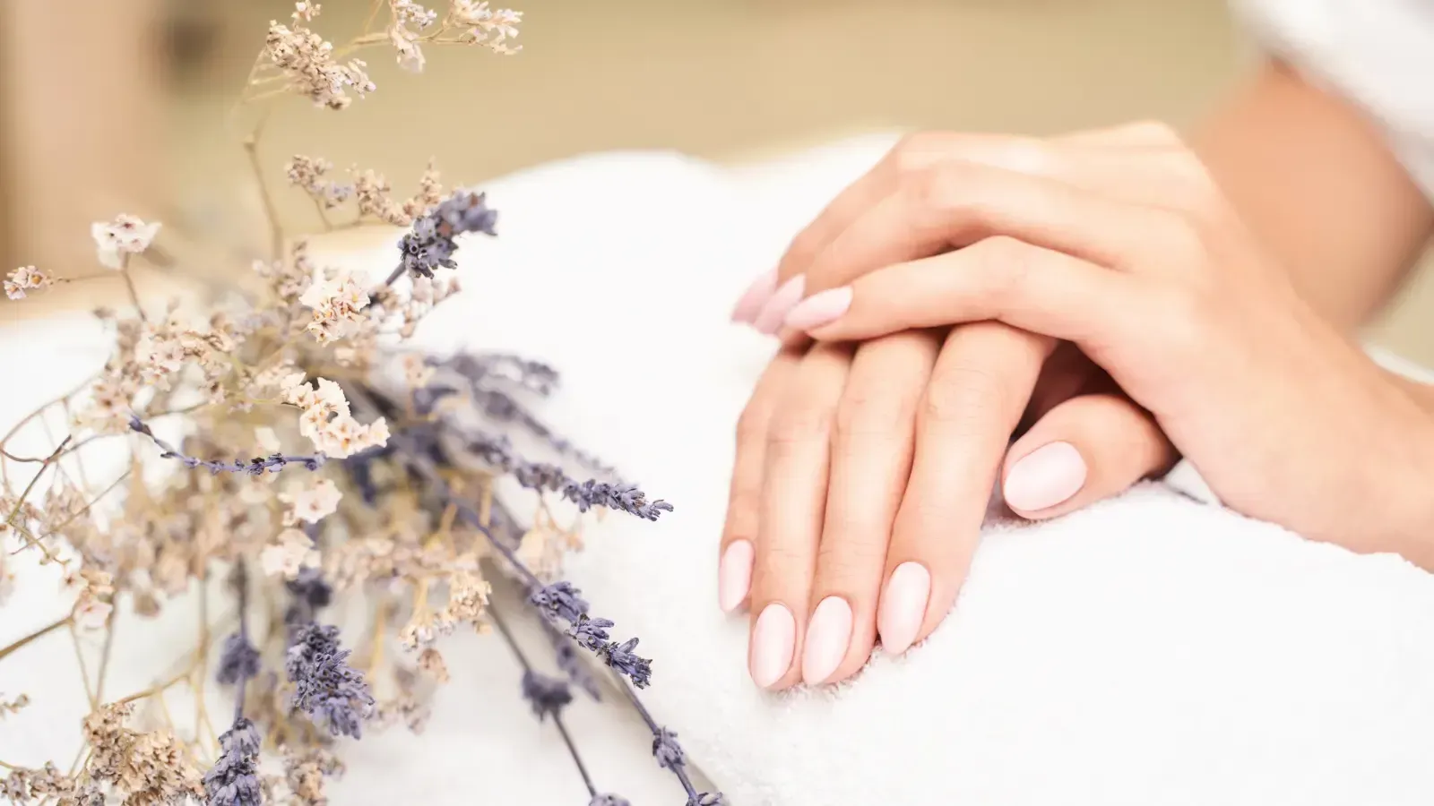 Close-up of manicured hands with pale pink nails resting beside delicate dried flowers