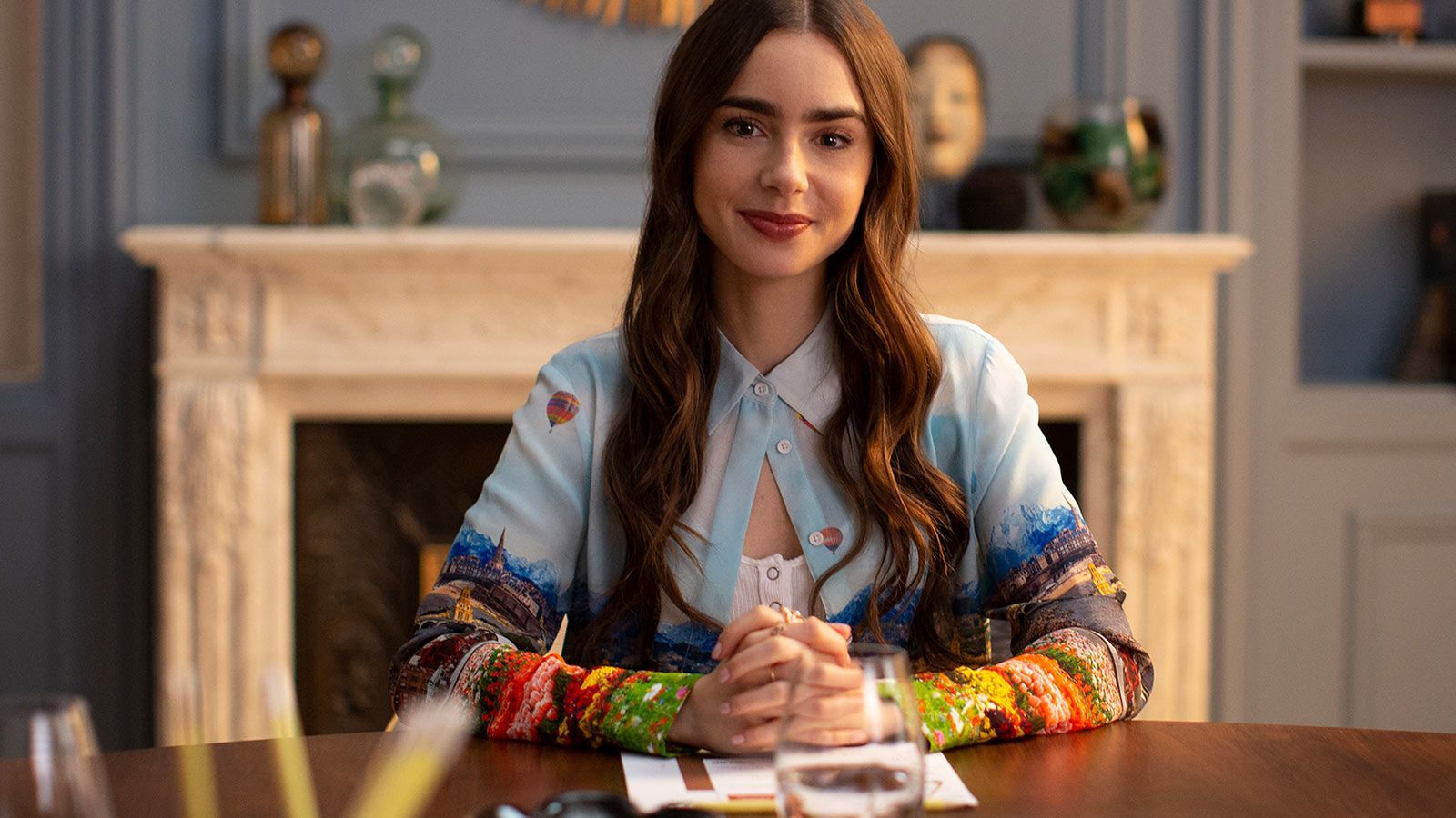 `Lily Collins as Emily Cooper sitting at a conference table with clasped hands in a stylish Parisian interior`
