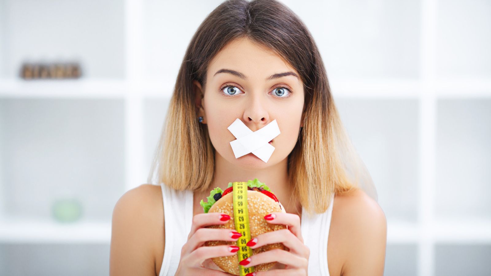 `Woman with taped mouth holding a burger wrapped in a measuring tape`