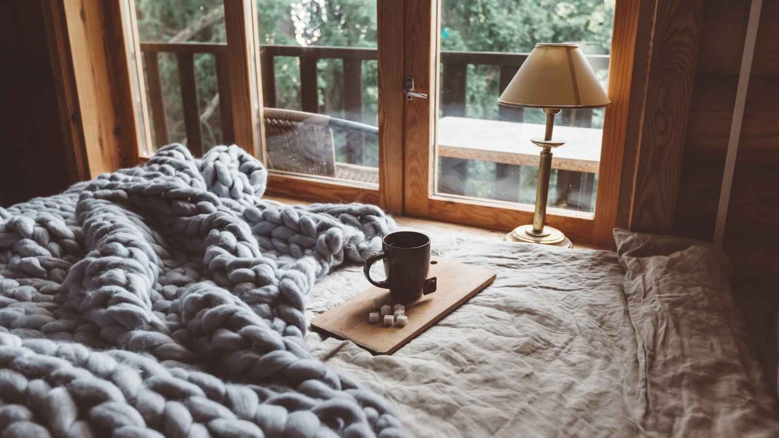 setting with bed with a cup of coffee on top and big window