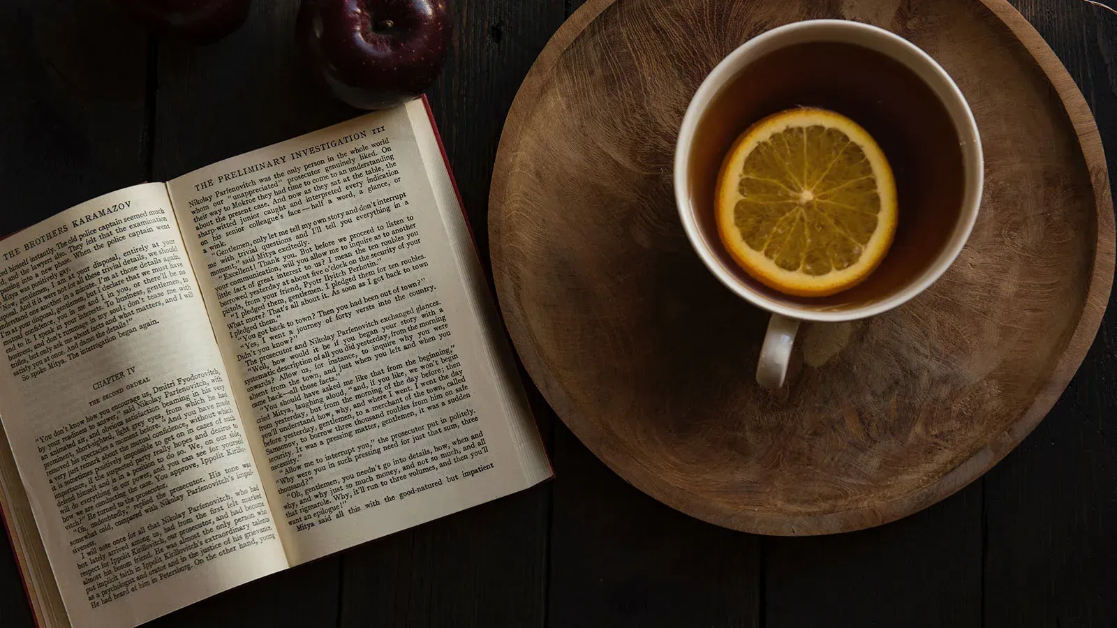 `Top-down view of an open hardcover book beside a cup of citrus tea with a lemon slice on a wooden coaster`