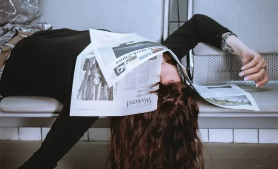 woman lays in a bench with newspapers covering her face
