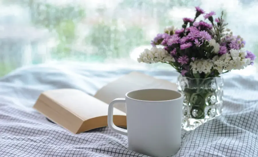 a book, a coffee and flower on a bed